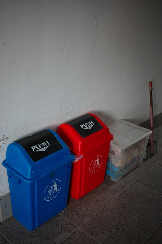 一个红色的垃圾桶坐在房间的角落里 旁边是一个蓝色的垃圾桶。
