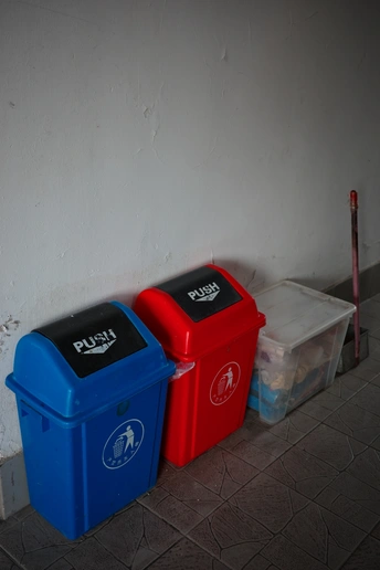 一个红色的垃圾桶坐在房间的角落里 旁边是一个蓝色的垃圾桶。