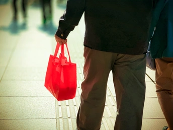 一个人手里拿着一个红色书包在地铁走廊上走 周围还有其他人经过。