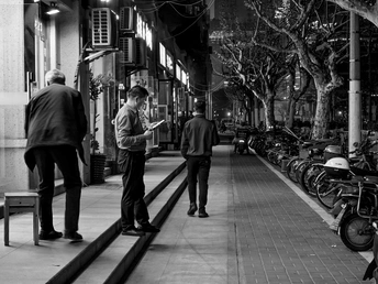 一张黑白照片 一些人在夜晚沿着人行道走 而一个人正在看手机。