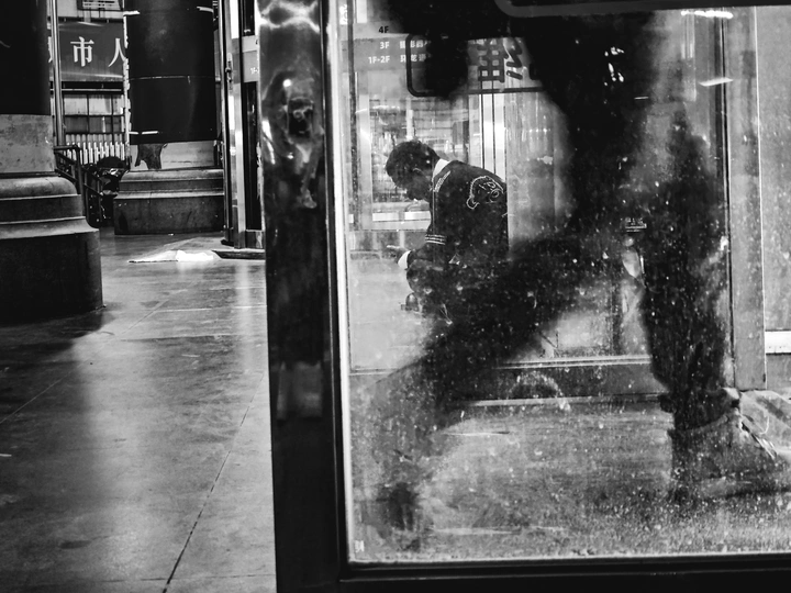 一个黑白照片 一个站在公交车站的男人 人们在他身边走过。