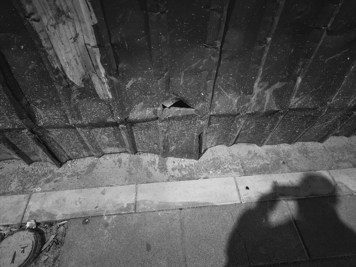 一个人在老建筑旁边人行道上行走的黑白色阴影