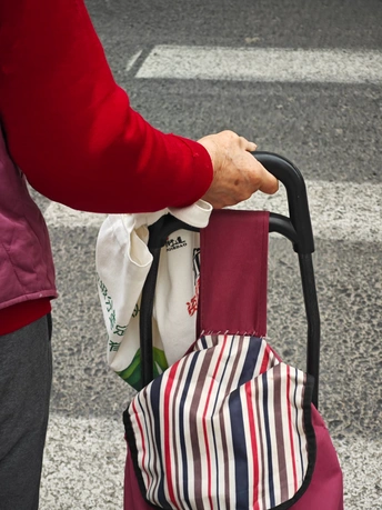 一位女士拿着红伞推着一个行李箱过人行横道