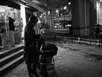 一张黑白照片 一个男子站在夜晚人行道上 旁边有一辆自行车。