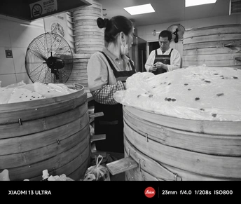 一张黑白照片 展示人们在面包店工作 旁边有一个大桶食物。