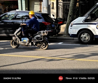 一个穿着黄色安全背心的男人骑摩托车在停有汽车的城市街道上。