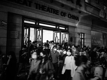 一张黑白照片 许多人站在一栋建筑前行走。