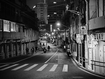 一张黑白照片 夜晚的街道 人们骑自行车和摩托车。