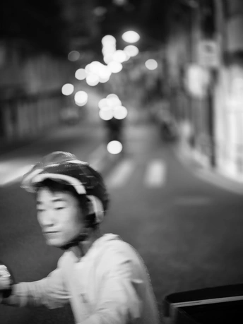 一张黑白照片 一个年轻男孩在夜晚骑街 手持棒球棒 戴着头盔。