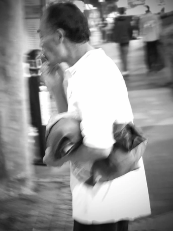 一张黑白照片 一个男子拿着一个包 一只狗在街上走 同时一个女子拿着一把伞。