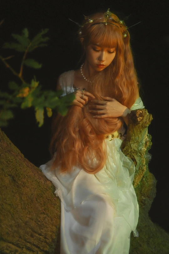 一个红头发的女孩穿着白色裙子坐在黑暗中的一棵树上 长发披肩。