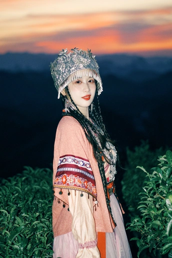 一位穿着传统服装的女士戴着帽子站在一个有山丘背景的田野中