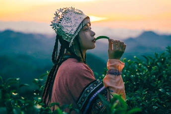 一个穿着民族服装的年轻女子 嘴里叼着烟管 在日落时的田野中。