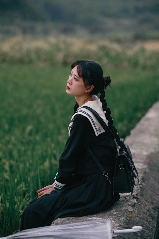 一个年轻女子坐在草地上 墙上 看书。