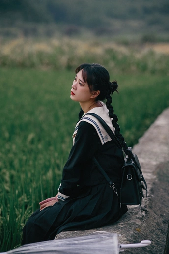 一个年轻女子坐在草地上 墙上 看书。