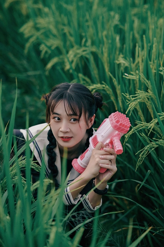 一位年轻女子手持粉色枪在一片高草丛中