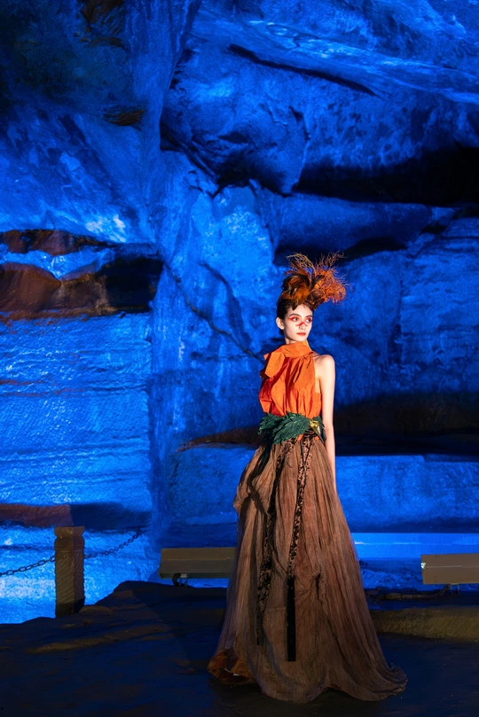 一位穿着橙色裙子的女人站在一个蓝色洞穴里