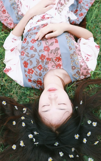 一个年轻女子躺在草地上 她的头发上插着花。
