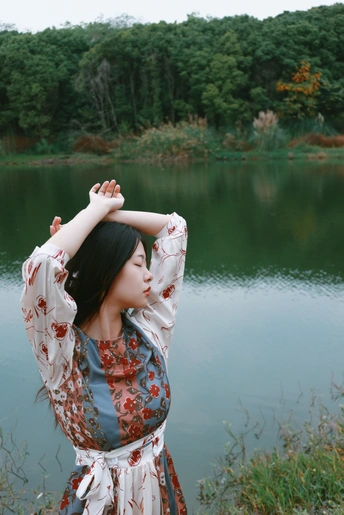 一位穿着漂亮裙子的年轻女子站在池塘前 双手在水里。