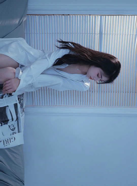 一个穿着白衬衫的年轻女子靠在一扇有百叶窗的房间里