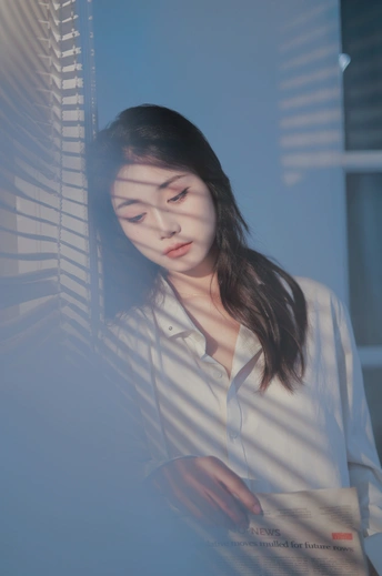 一位年轻女子穿着白色衬衫 正在透过窗帘凝视窗外。