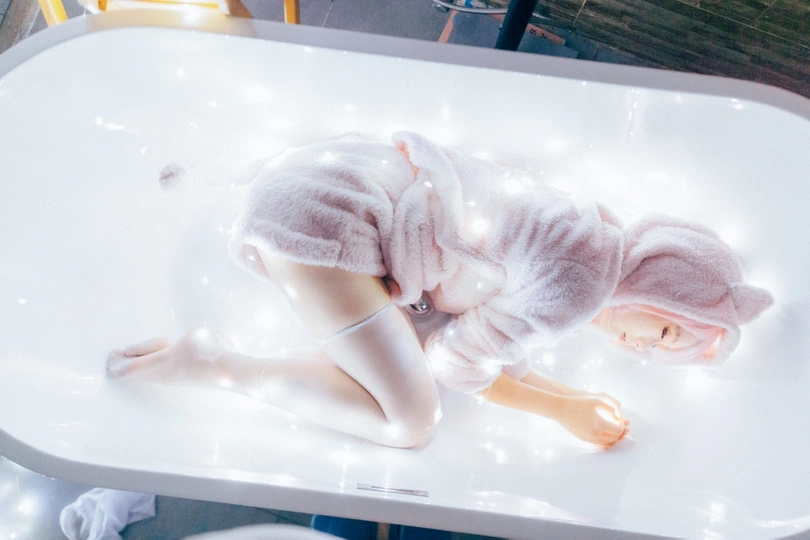 一个躺在浴缸里的洋娃娃 上面盖着一条白毛巾 还有一个装有灯的桌子。