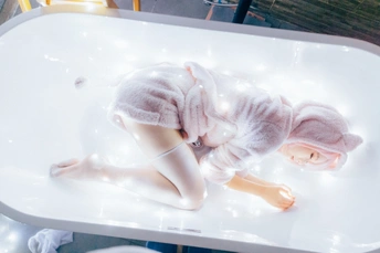 一个躺在浴缸里的洋娃娃 上面盖着一条白毛巾 还有一个装有灯的桌子。