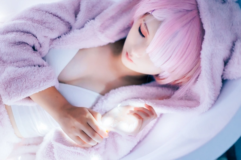 一个留着粉红色头发的年轻女子躺在白色毛毯下