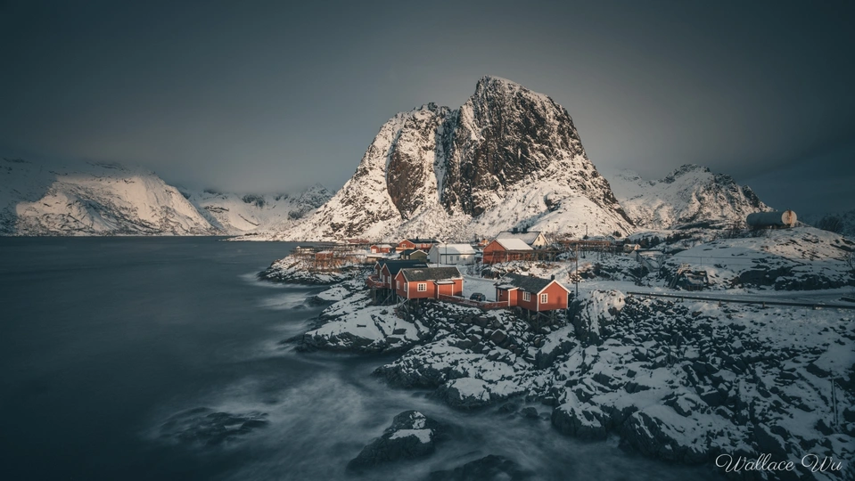一个位于峡湾中的岛屿上的小村庄 背景是白雪皑皑的山峰。