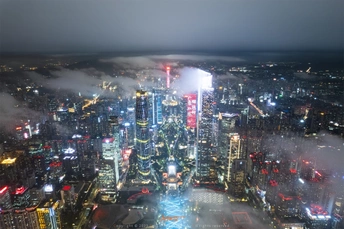 夜幕下城市景观的空中视角 摩天大楼凌驾于云层之上 雾气缭绕。