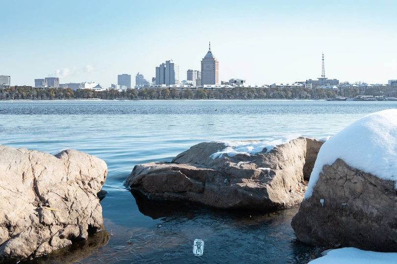 湖面结冰 岩石上有雪和冰 背景中有一座城市。