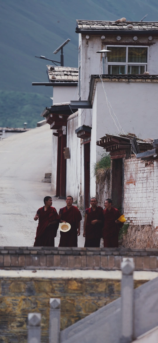 穿着长袍的人在乡村小路上行走 背景有建筑和水。