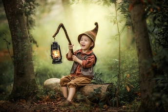 一个穿着巫师服装的年轻男孩或女孩坐在森林里拿着灯笼。