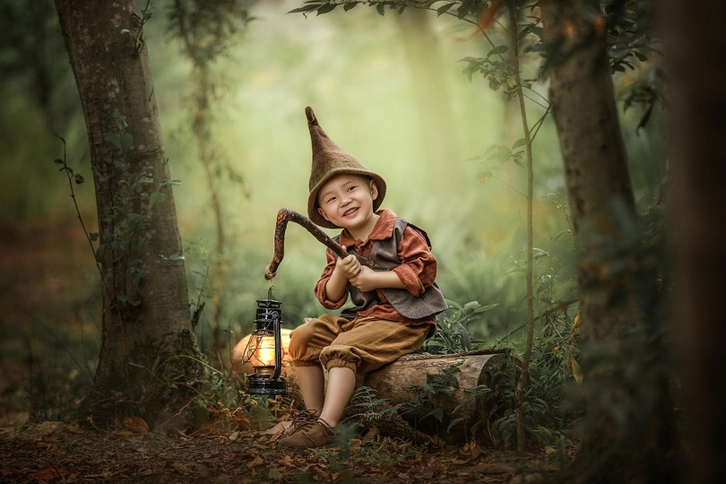 一个小男孩穿着女巫装坐在森林里拿着灯笼