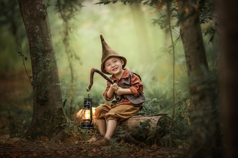 一个小男孩穿着女巫装坐在森林里拿着灯笼