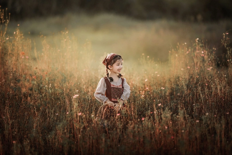 一个小女孩穿着裙子站在一片高草花丛中