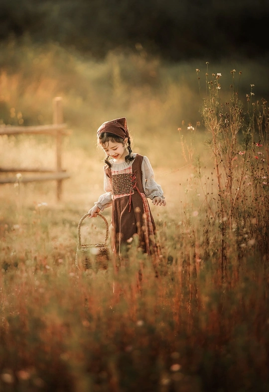 一个小女孩穿着裙子、帽子 带着篮子在田野里。