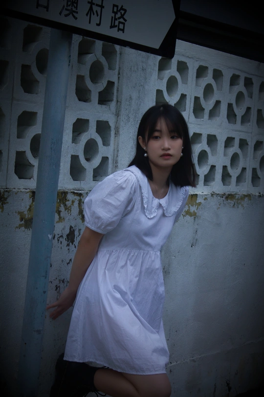 一位穿着白色连衣裙的年轻女子站在一面墙前