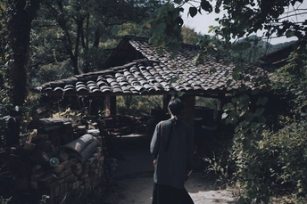 一个人站在森林中的一条小径上 靠近一所房子。