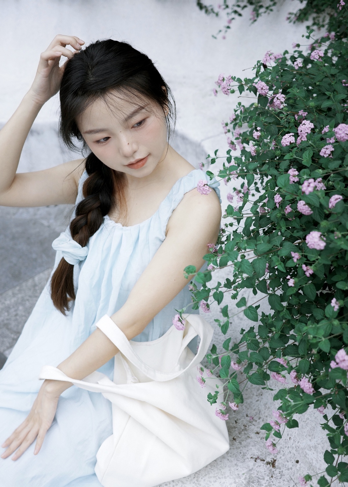 一个穿着白色连衣裙的年轻女子坐在墙上 她的头发上插着花。