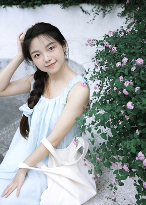 一位穿着蓝色连衣裙的年轻女子坐在白色墙壁旁 头戴鲜花。