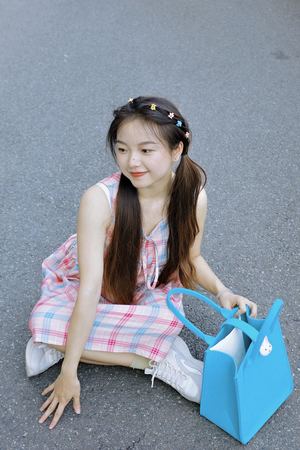 一个穿着裙子的年轻女孩抱着一个蓝色包包坐在地板上