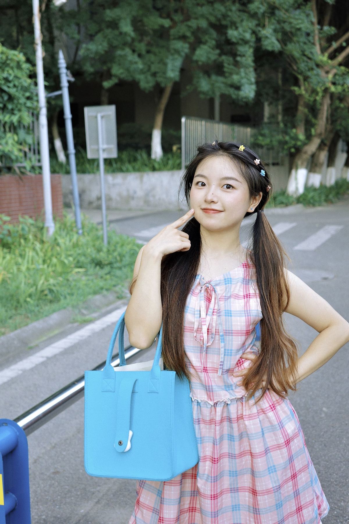 一位穿着连衣裙的年轻女子拿着一个蓝色包包站在街上
