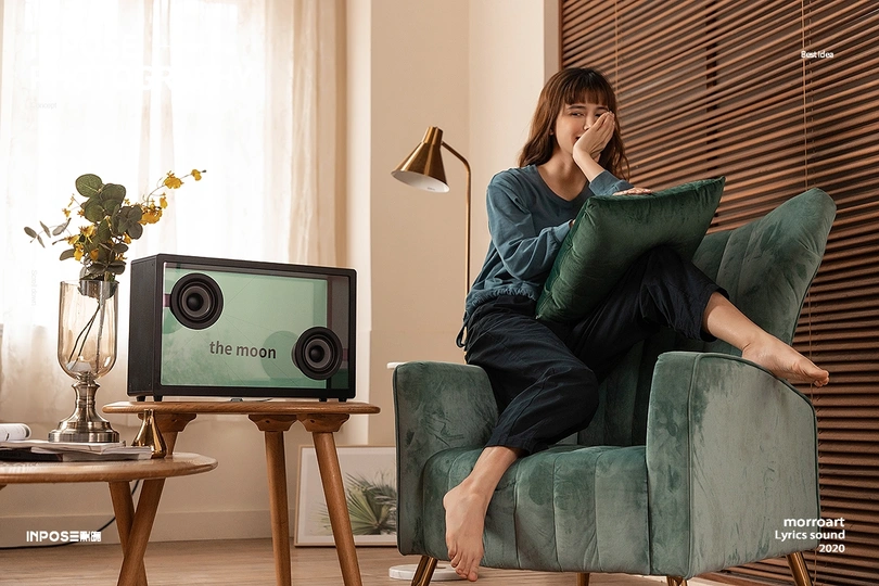 一个坐在绿色椅子上 周围有电视和扬声器的客厅里的女人 还有一个枕头。