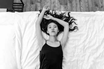 一张黑白照片 一位年轻女子躺在床上 床单是白色的。