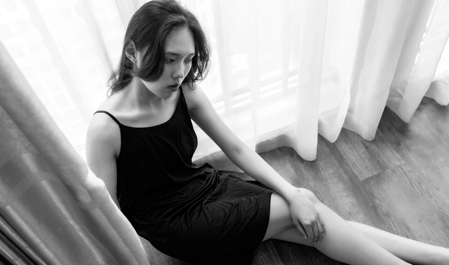 一张黑白照片 一位年轻女子坐在地板上 双腿交叉在窗户前