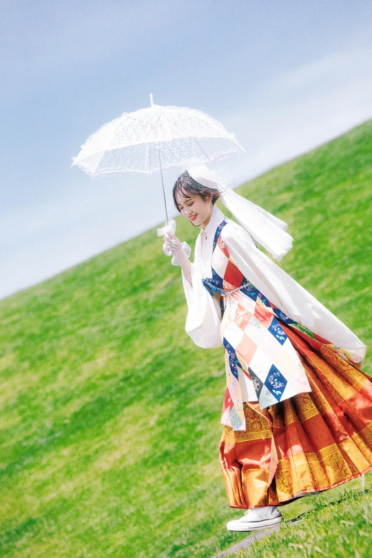 一位穿着传统服装的年轻女子手持白色雨伞穿越草地上的小山丘。