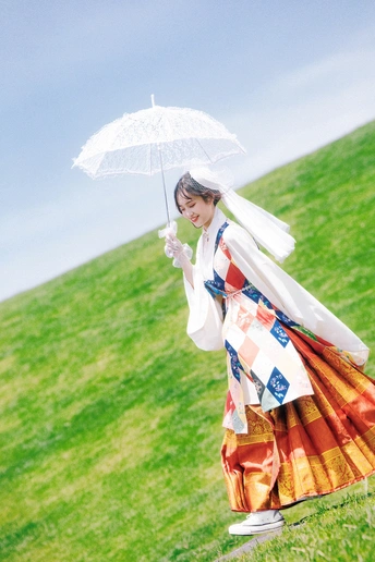 一位穿着传统服装的年轻女子手持白色雨伞穿越草地上的小山丘。