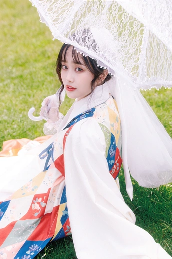 一位穿着传统服装的年轻女子 戴着白色面纱 手持雨伞 坐在草地上。