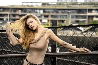 一位年轻女子站在桥上 倚靠在围栏上 头发被风吹得梳理整齐。